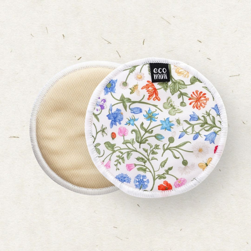 Two round reusable cloth breast pads on a light beige textured background. One wipe is open, showing a soft beige fabric side, while the other is closed, displaying a white cover decorated with a colorful embroidered floral pattern and a small black 'eco mini' brand label.