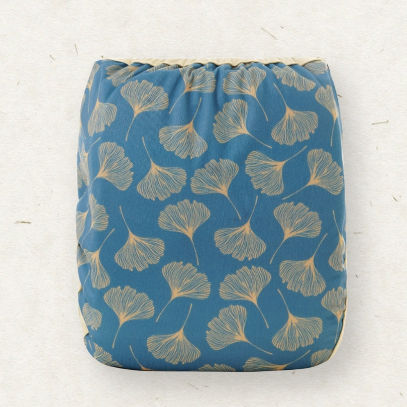 A square fabric pouch with a drawstring top, featuring a repeating pattern of light beige ginkgo leaves on a medium blue background, set against a textured off-white backdrop.