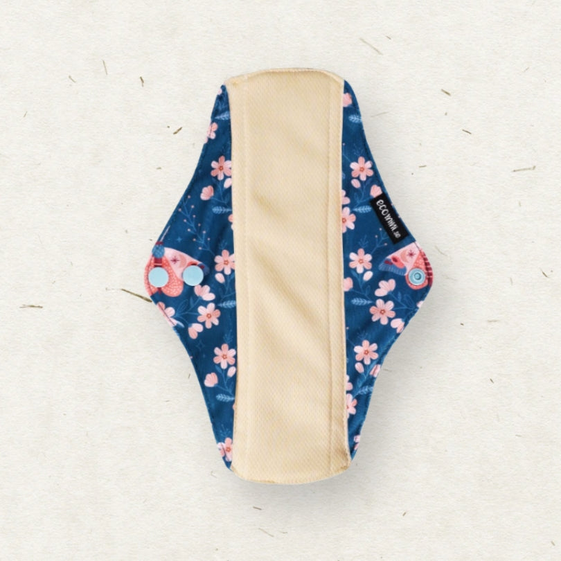 A reusable menstrual pad with a navy blue floral pattern featuring pink cherry blossoms and small red flowers, with a beige fabric lining in the center, shown on a textured off-white background.