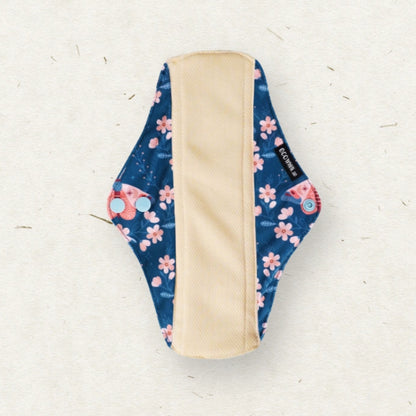 A reusable menstrual pad with a navy blue floral pattern featuring pink cherry blossoms and small red flowers, with a beige fabric lining in the center, shown on a textured off-white background.