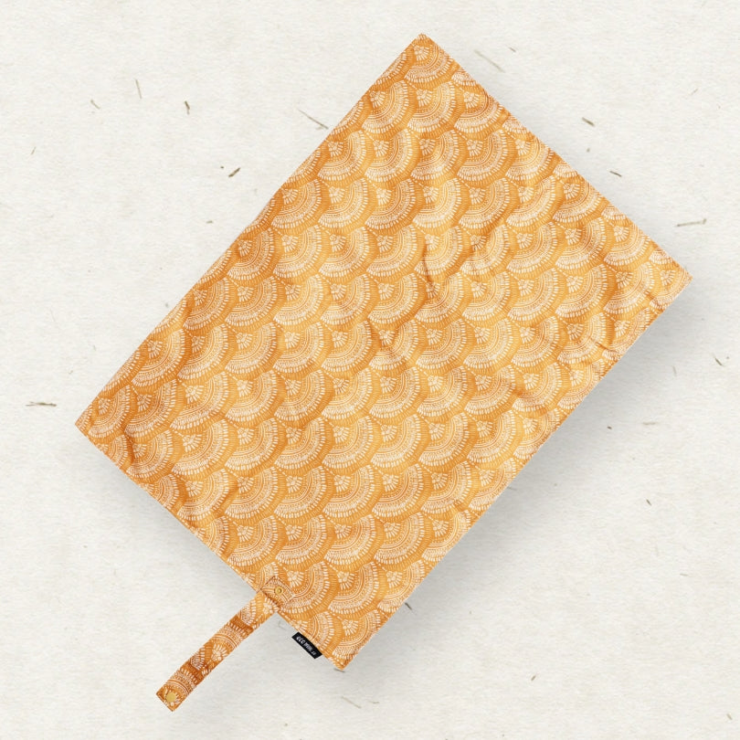 Eco Mini Changing mat/ Skötunderlägg -  with a repeating scallop-scale pattern in warm orange and beige, shown on a light textured background.