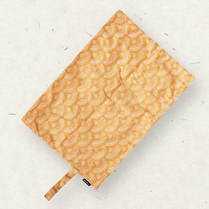 Eco Mini Changing mat/ Skötunderlägg -  with a repeating scallop-scale pattern in warm orange and beige, shown on a light textured background.