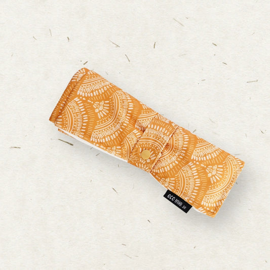 Eco Mini Changing mat/ Skötunderlägg - with an orange and white mandala pattern, placed diagonally on a textured off-white background with small scattered fibers.