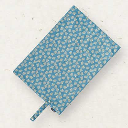 A diaper changing mat in a medium blue fabric with a repeating light beige abstract pattern, shown on a textured off-white background.