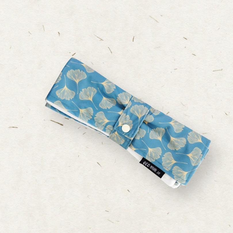 A blue fabric changing mat with a beige ginkgo leaf pattern, featuring a snap-button closure and a black brand label that reads 'ECO MINI'.