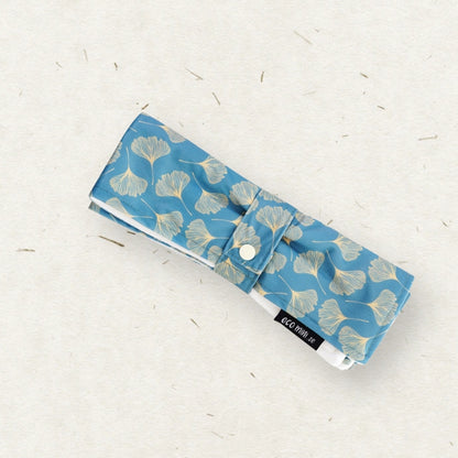 A blue fabric changing mat with a beige ginkgo leaf pattern, featuring a snap-button closure and a black brand label that reads 'ECO MINI'.