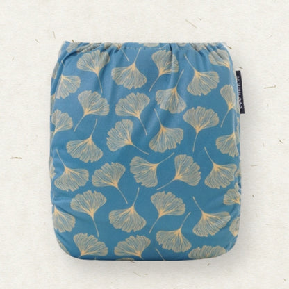 A square reusable cloth pad with a blue background and a beige ginkgo leaf pattern, shown flat against a light textured background.