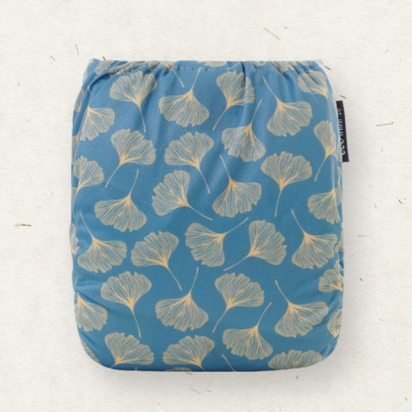A square reusable cloth pad with a blue background and a beige ginkgo leaf pattern, shown flat against a light textured background.