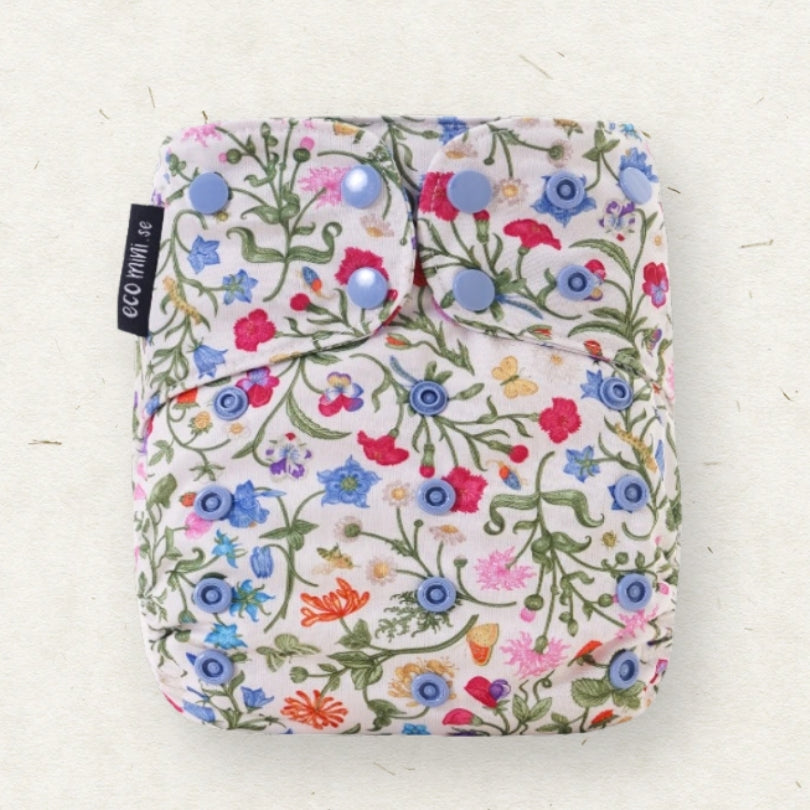 A reusable cloth diaper with a colorful wildflower print on a white background, featuring three light blue snap buttons and a black fabric tag on the side.