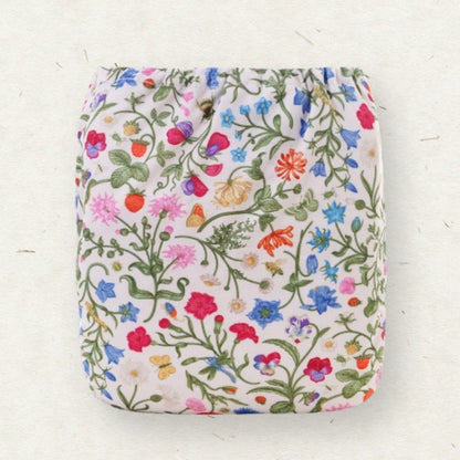 A reusable cloth diaper with a dense, colorful wildflower and butterfly pattern on a cream background, displayed flat against a textured off-white surface.