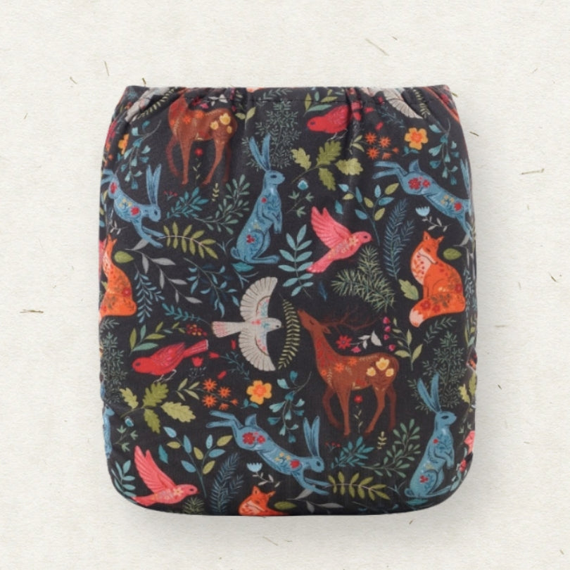A square reusable cloth diaper with a dark background and a colorful woodland animal print featuring foxes, rabbits, birds, and leaves.
