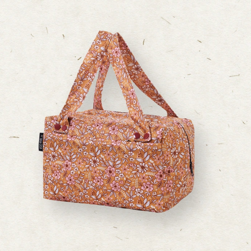 Eco Mini Cloth Diaper POD - with a warm orange-brown base and an all-over pink, white, and muted green floral print, featuring dual top handles and a small black side tag, set against a textured off-white background.