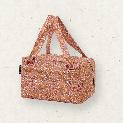 Eco Mini Cloth Diaper POD - with a warm orange-brown base and an all-over pink, white, and muted green floral print, featuring dual top handles and a small black side tag, set against a textured off-white background.