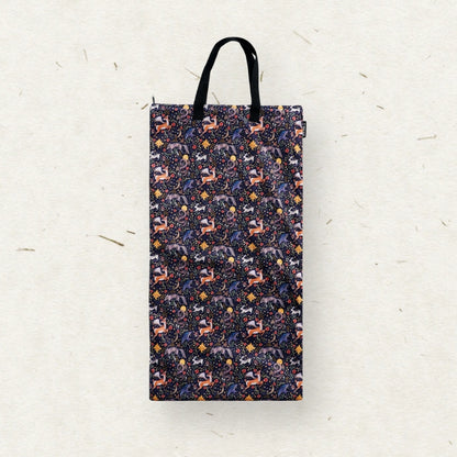 A tall rectangular Eco Mini brand wet bag with black handles, featuring a dense all-over pattern of stylized forest animals in purple, orange, and white on a dark navy background, set against a textured off-white paper backdrop.