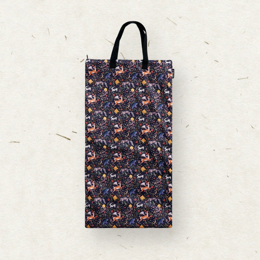 A tall rectangular Eco Mini brand wet bag with black handles, featuring a dense all-over pattern of stylized forest animals in purple, orange, and white on a dark navy background, set against a textured off-white paper backdrop.