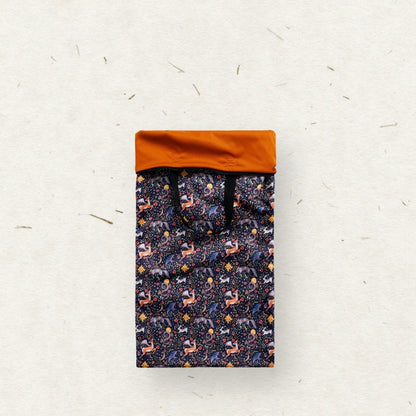 A tall rectangular Eco Mini brand wet bag with black handles, featuring a dense all-over pattern of stylized forest animals in purple, orange, and white on a dark navy background, set against a textured off-white paper backdrop.