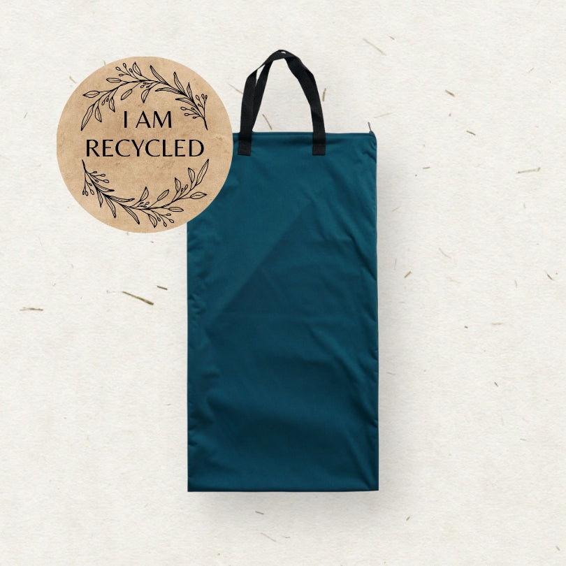 A dark teal Eco mini Large cloth diaper wet bag/ PUL påse with black handles, shown on a textured off-white background with a circular 'I AM RECYCLED' graphic overlay in the top left.