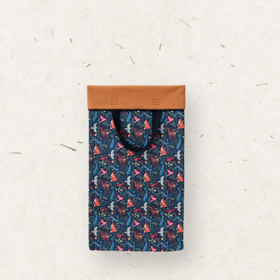 A wet bag with black handles, featuring a dark blue and pink patterned body, laid flat on a textured off-white background.