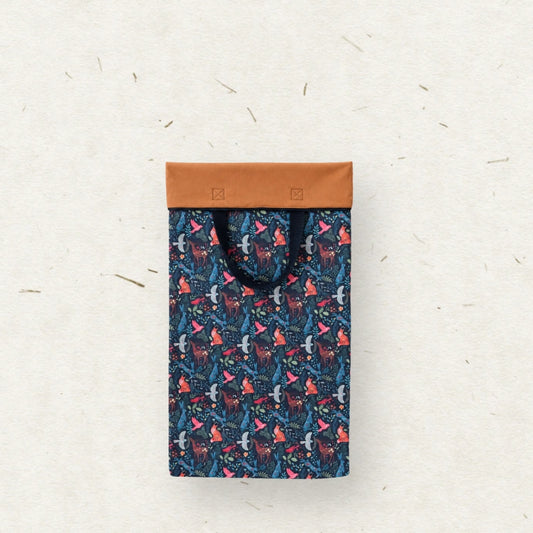 A wet bag with black handles, featuring a dark blue and pink patterned body, laid flat on a textured off-white background.
