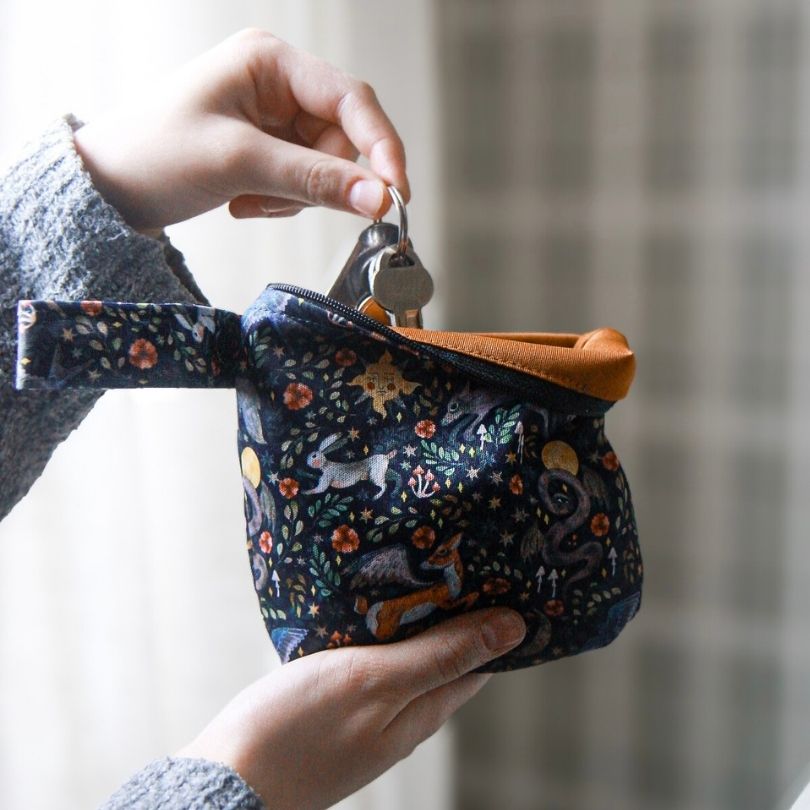 Hand holding a small Eco Mini wet bag with keychain, featuring animal prints on a dark background.