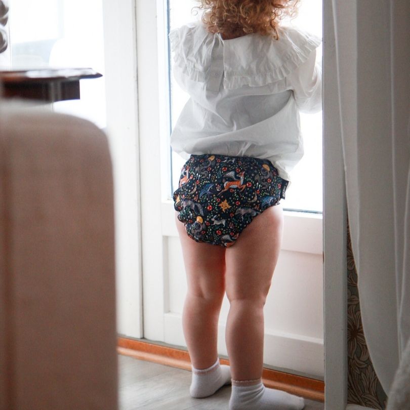 Person wearing a white shirt and patterned Eco Mini cloth diaper standing by a window.