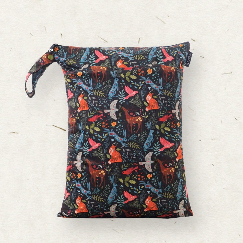 A cloth diaper wet bag with a colorful woodland animal print on a dark background, featuring a carrying loop on the left side, photographed flat against a light textured background.