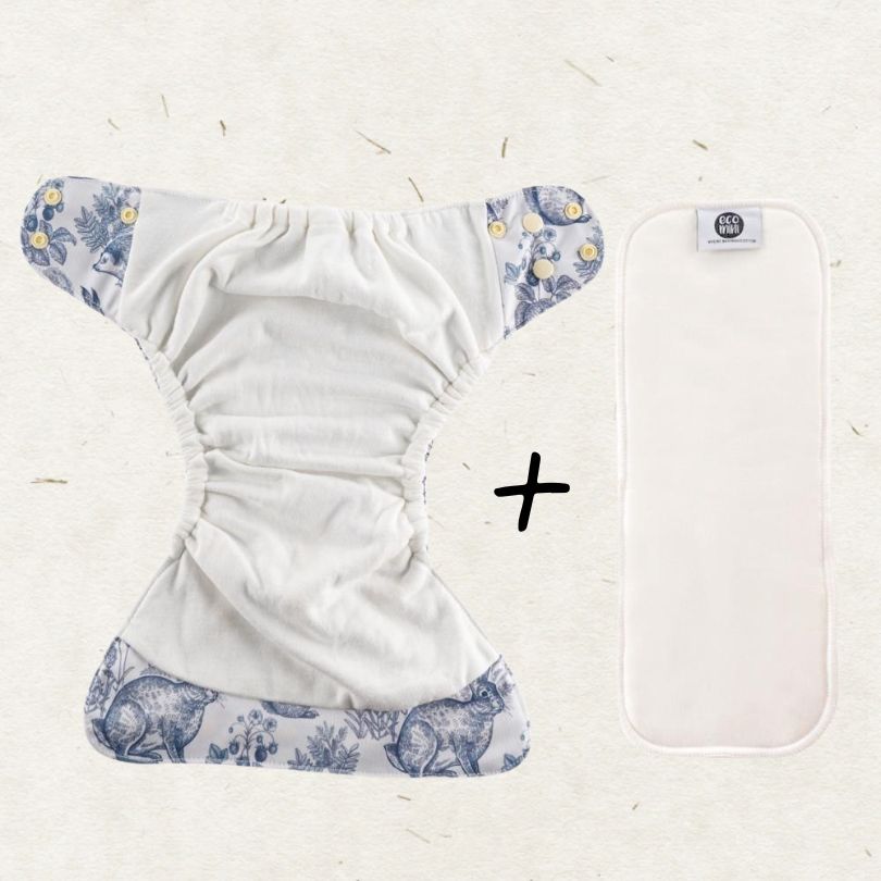 A reusable cloth diaper with blue floral and animal-print trim on a light beige textured background, shown next to an additional white insert pad with a small visible 'Eco Mini' label.