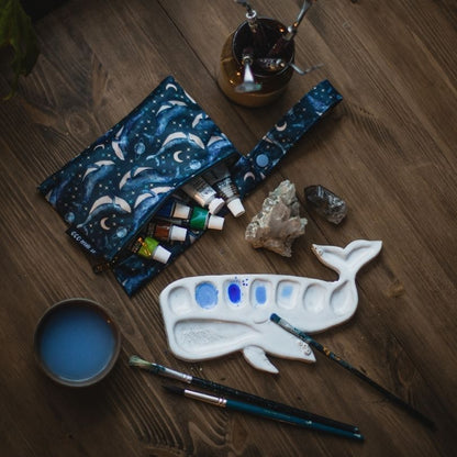 Art supplies including a whale-shaped palette, paintbrushes, and a Eco Mini wet bag with whale pattern on a wooden surface.