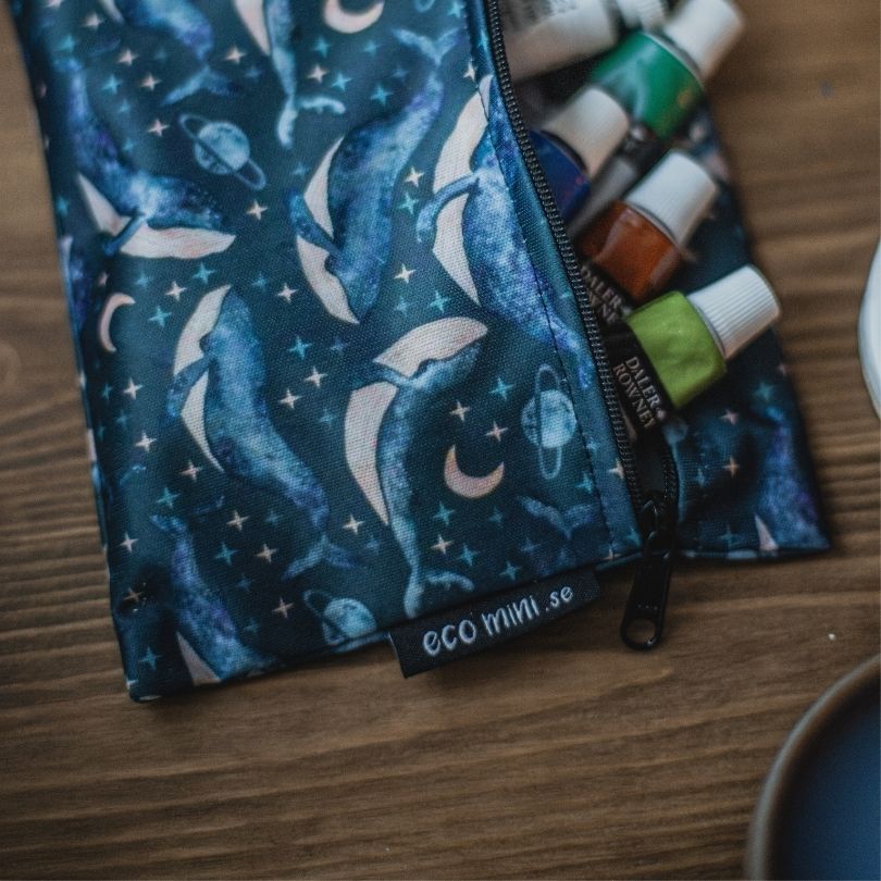 Eco Mini wet bag with whale pattern containing art supplies on a wooden surface