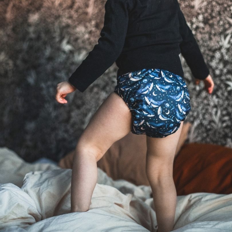 Person wearing an Eco Mini whale patterned cloth diaper standing on a bed.
