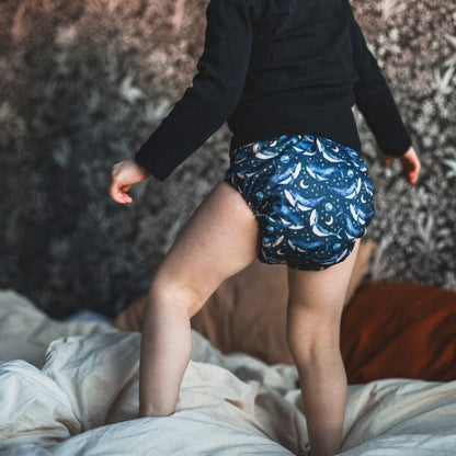 Person wearing a blue patterned Eco Mini cloth diaper standing on a bed.
