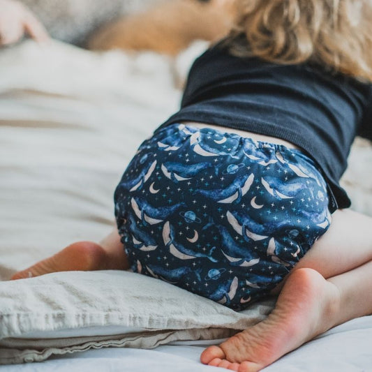Child wearing a blue patterned Eco Mini cloth diaper on a bed