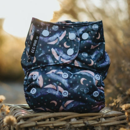 Patterned Eco Mini cloth diaper on a woven surface with a blurred natural background