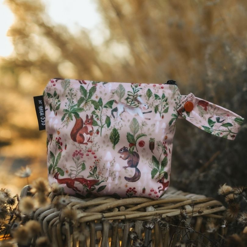 Floral-patterned Eco Mini wet bag with animal designs on a woven surface with a blurred natural background