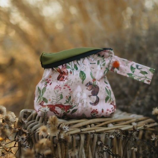 Floral-patterned Eco Mini wet bag with animal designs on a woven surface with a blurred natural background