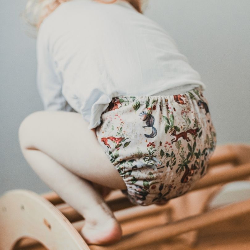 Child wearing an Eco Mini floral-patterned diaper on a wooden chair with a neutral background