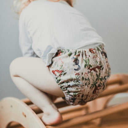 Child wearing an Eco Mini floral-patterned diaper on a wooden chair with a neutral background