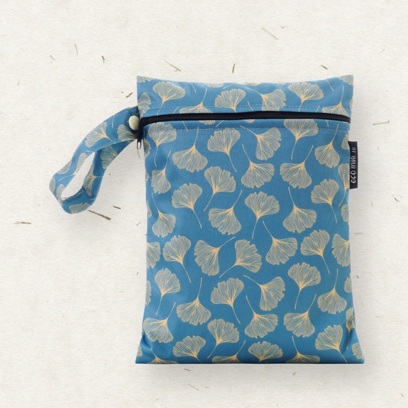 A blue fabric wet bag with a repeating ginkgo leaf pattern, featuring a top zipper, a matching wrist strap, and a small black brand tag reading ECO MINI, set against a textured off-white background.