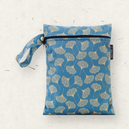 A blue fabric wet bag with a repeating ginkgo leaf pattern, featuring a top zipper, a matching wrist strap, and a small black brand tag reading ECO MINI, set against a textured off-white background.