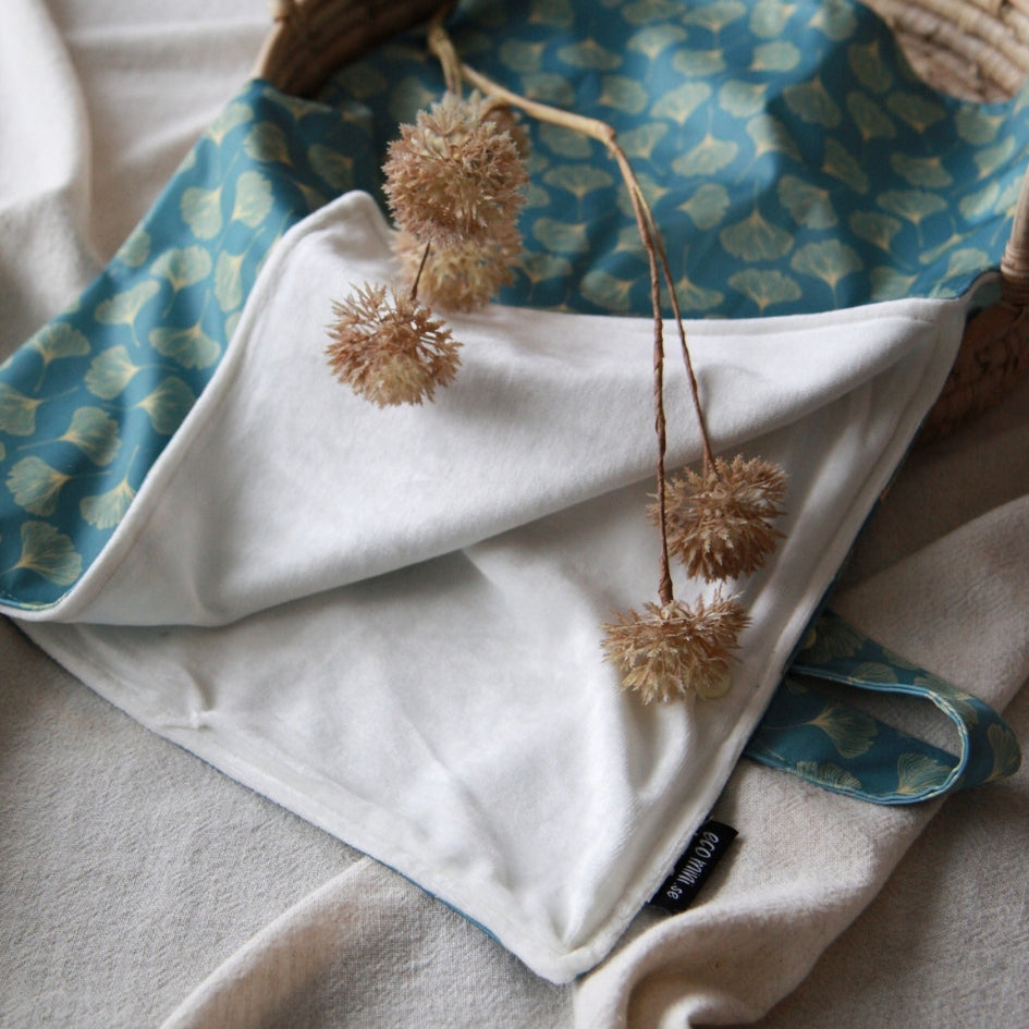 A soft cloth diaper changing mat with a blue and beige patterned reverse side, styled with dried flower stems on a neutral fabric background.